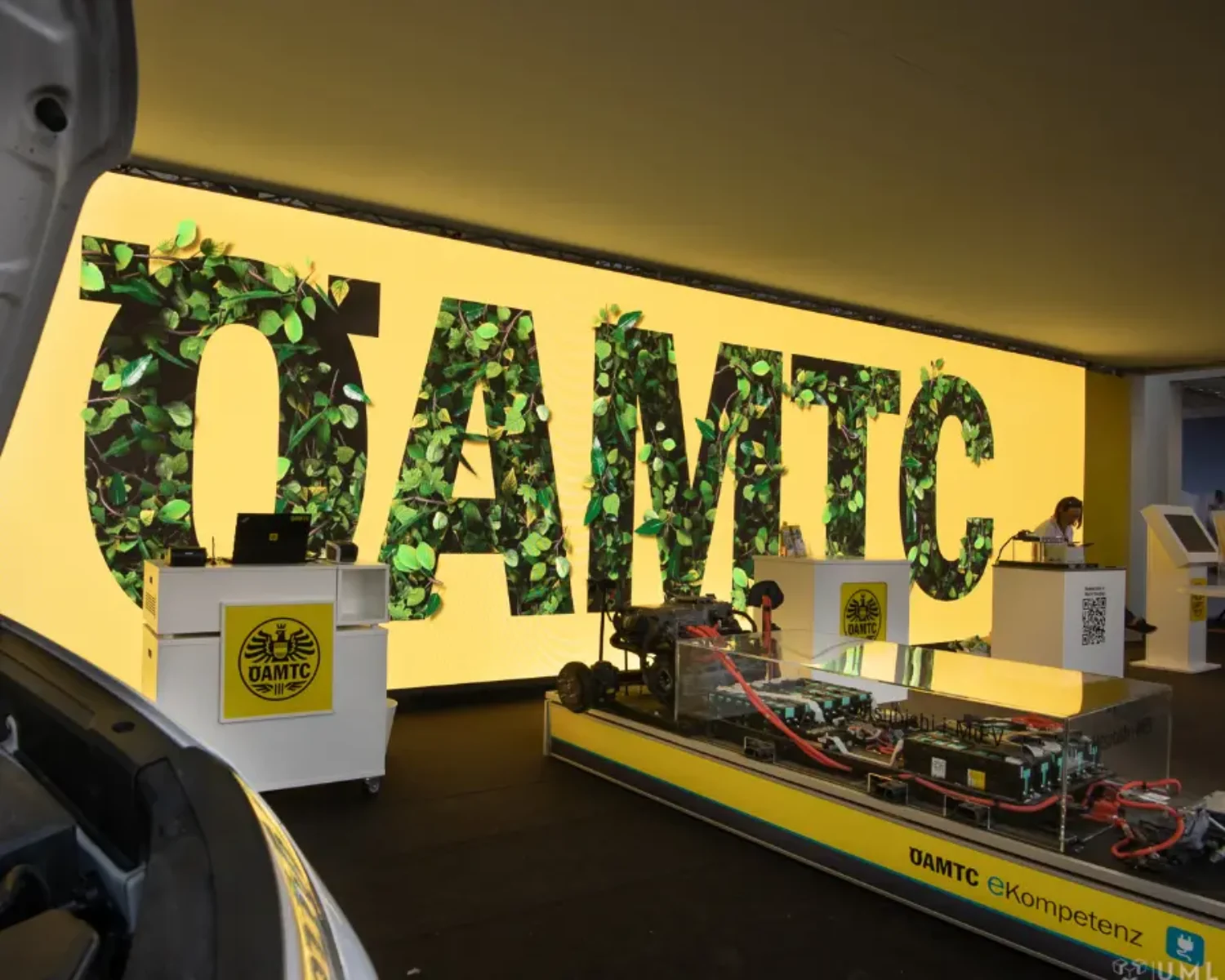 A big LED screen at an exhibition booth, showing growing ivy covering the oeamtc Logo. 3D particle animation with photorealistic leaves.